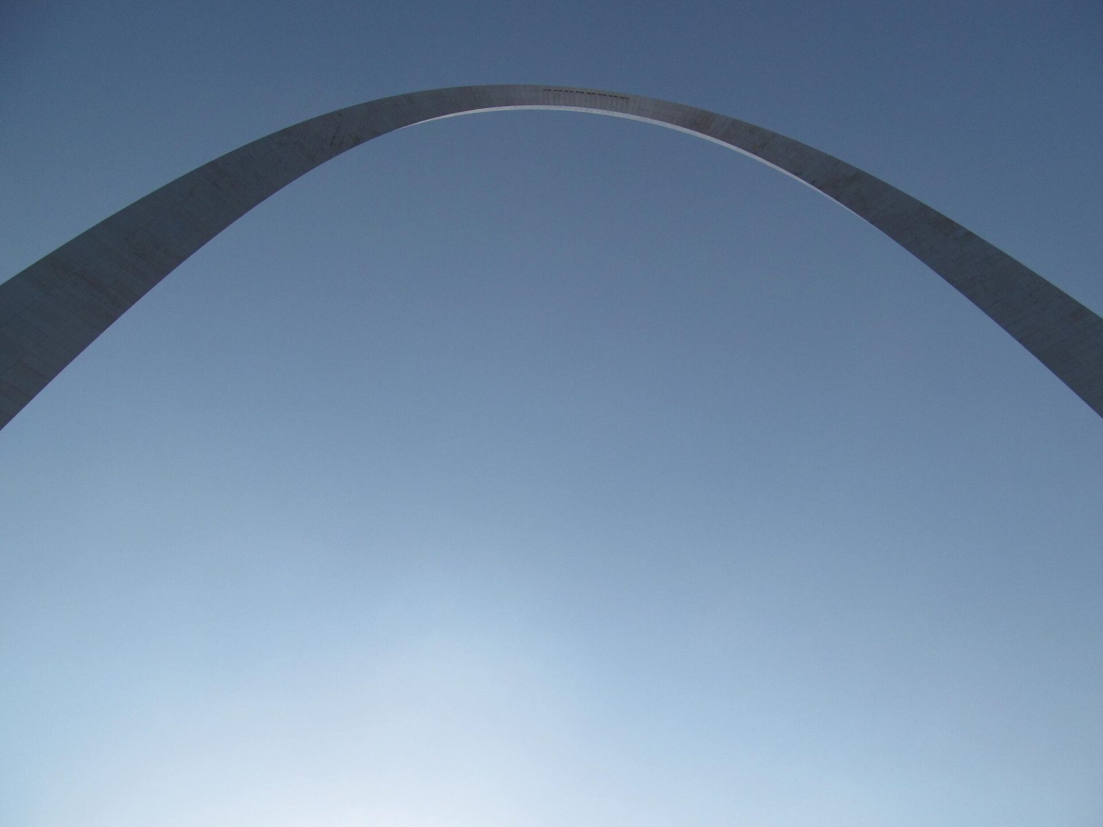 The underside of the Gateway Arch against a clear blue sky, the stainless steel curve filling the frame